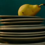 A stack of dirty plates with a ripe yellow pear balanced on top, symbolizing imbalance or a messy workload.