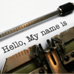 Close-up of a vintage typewriter typing the words “Hello, My name is” on a sheet of white paper.