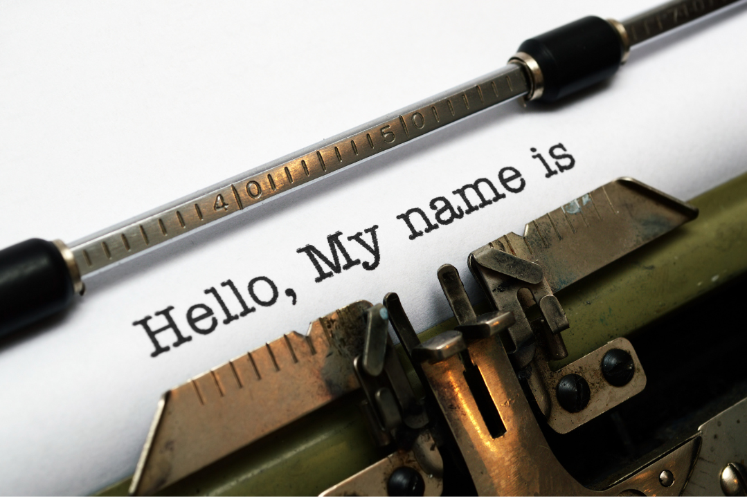 Close-up of a vintage typewriter typing the words “Hello, My name is” on a sheet of white paper.