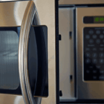 Close-up of a stainless steel over-the-range microwave with the door slightly open, symbolizing a recent appliance breakdown.